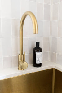 Bottle of dog shampoo with natural ingredients, sulphate and paraben free with spiced cucumber, lavender and tea-tree scent next to a sink with gold tap.